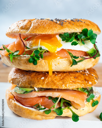 Healthy freshly baked bagel filled with salmon, microgreen, avocado and egg. Served on white desk. Sandwich with salmon. Healthy breakfast.