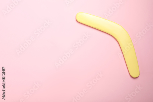 Yellow wooden boomerang on pink background, top view. Space for text