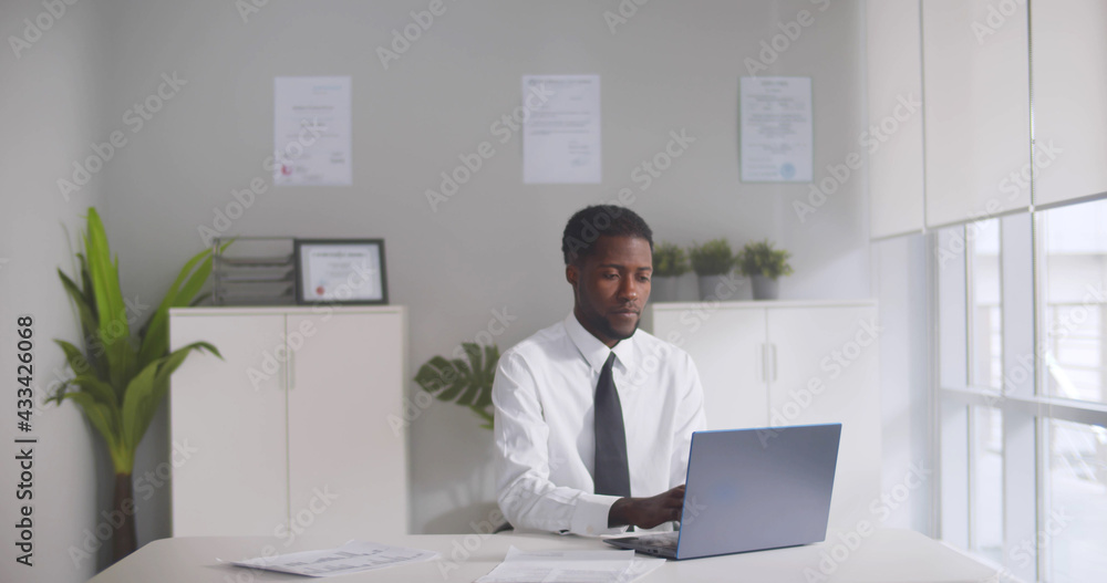 Afro-american businessman working on laptop at desk in office Afro-american businessman working on laptop at desk in office