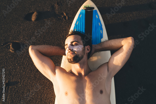 Foto Muscular eyes closed man sunbathing on sandy beach during sunset