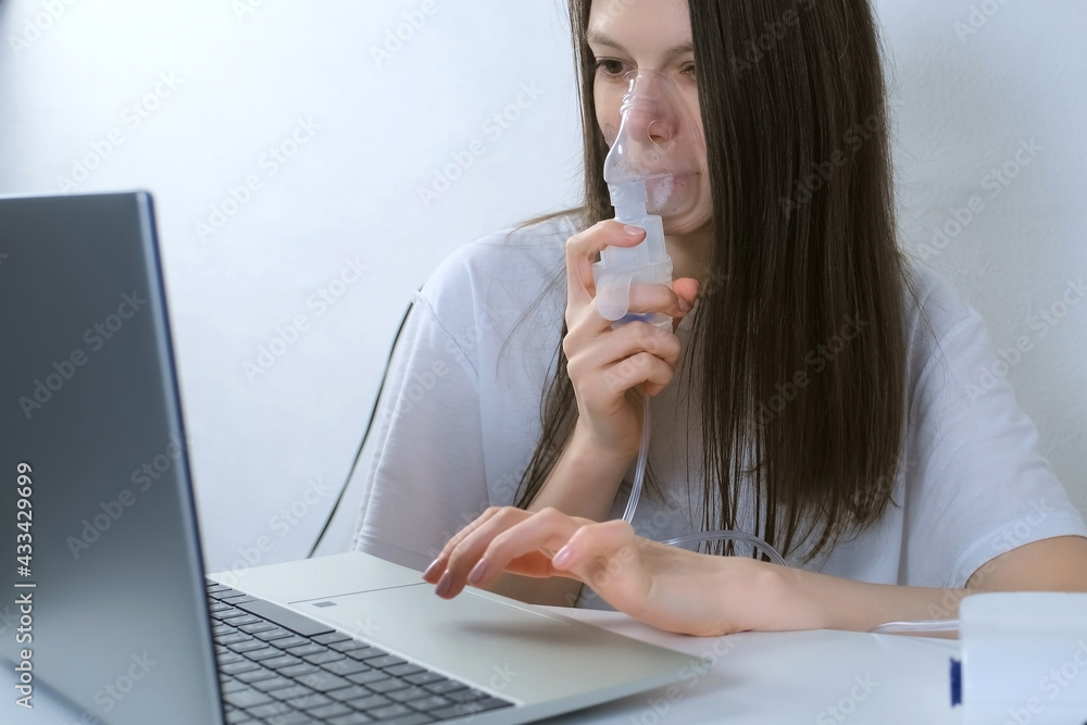 Sick young woman is using nebulizer and inhaler for treatment at home and working on laptop. She is breathing in mask. Fibrosis, covid-19, asthma, copd. Treatment, cure and procedure, therapy. Sick young woman is using nebulizer and inhaler for treatment at home and working on laptop. She is breathing in mask. Fibrosis, covid-19, asthma, copd. Treatment, cure and procedure, therapy.