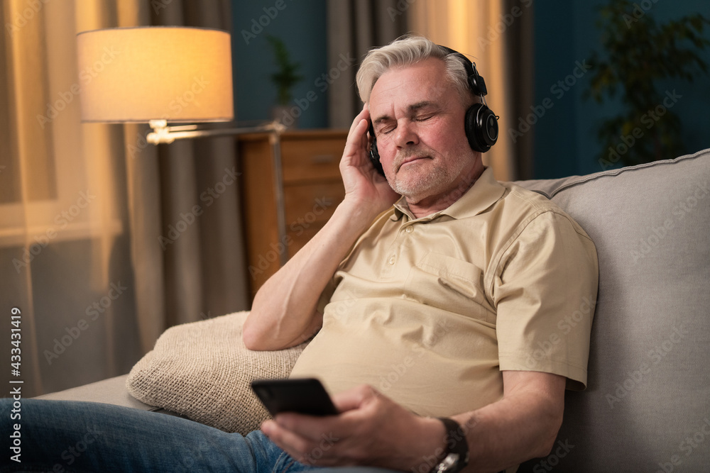 A retiree listens to music on headphones. A senior citizen uses wireless headphones. A man is listening to podcasts on headphones from his phone. An older man listens to his favorite music tracks.