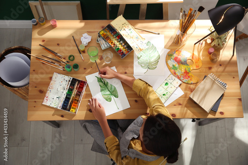 Billede på lærred Young woman drawing leaf with watercolors at table indoors, top view