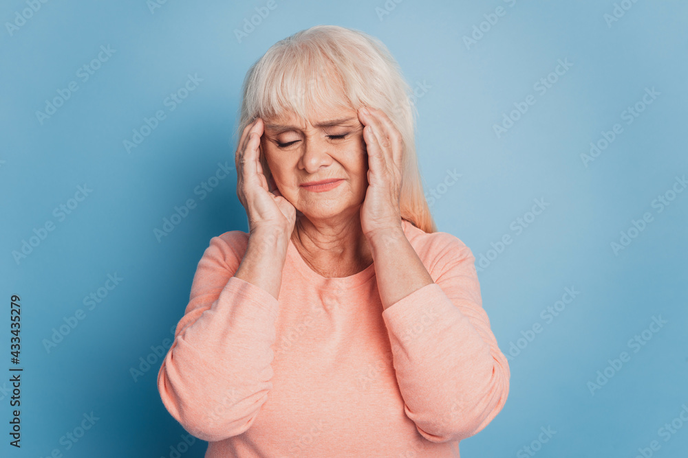 Mature woman with headache holding her temples feel unwell on blue backdrop Mature woman with headache holding her temples feel unwell on blue backdrop