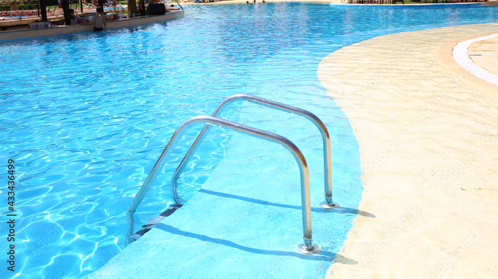 Background of blue transparent water in the swimming pool on the territory of the hotel. Descent to the pool with handrails. Rest and relaxation concept. Active rest by the sea.