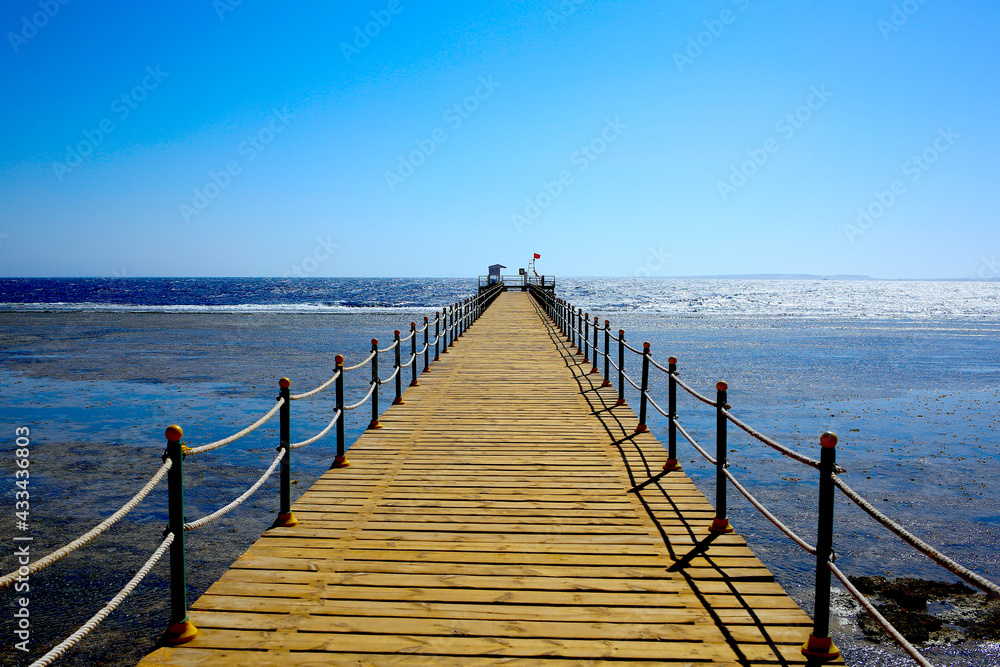 The skyline is where the wooden bridge leads to the pier. Red flag as a sign that the entrance is closed, it is dangerous to be in the sea. Sunset at the sea. Vacation concept
