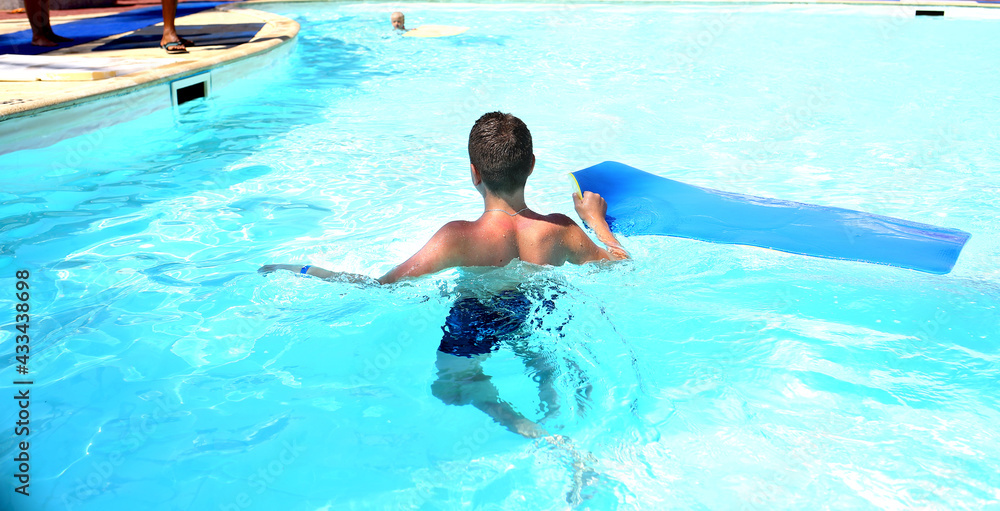 Banner with a teenage boy back view in the pool with a soft mat for descending from the water attraction. Entertainment for children. Recreation and tourism concept. Blue water background.