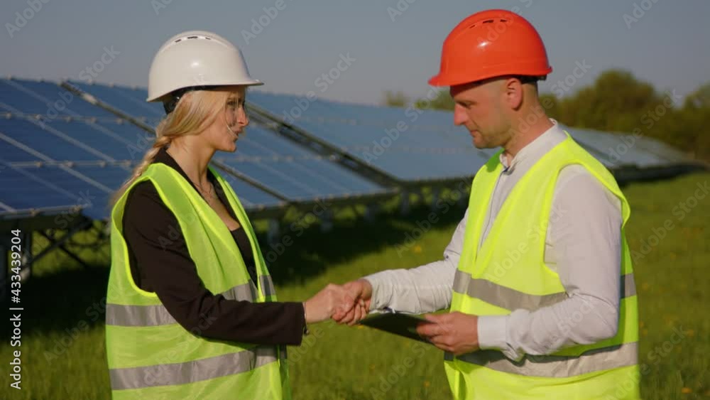 Two engineers are discussing drawings for the project. They are standing at a solar panel station. The female engineer is pointing with her hand to the object Two engineers are discussing drawings for the project. They are standing at a solar panel station. The female engineer is pointing with her hand to the object
