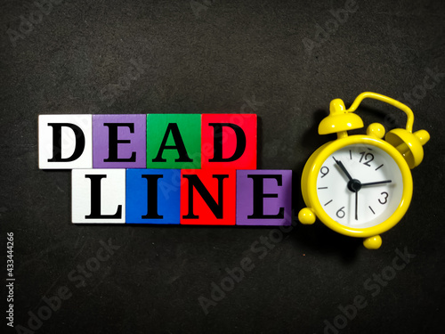 Text DEADLINE with colorful wooden jigsaw and alarm clock on black background.