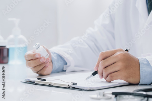 Doctor holding prescription bottle and writing prescription on special form at office room. Healthcare, Vaccine,medical and pharmacy concept.