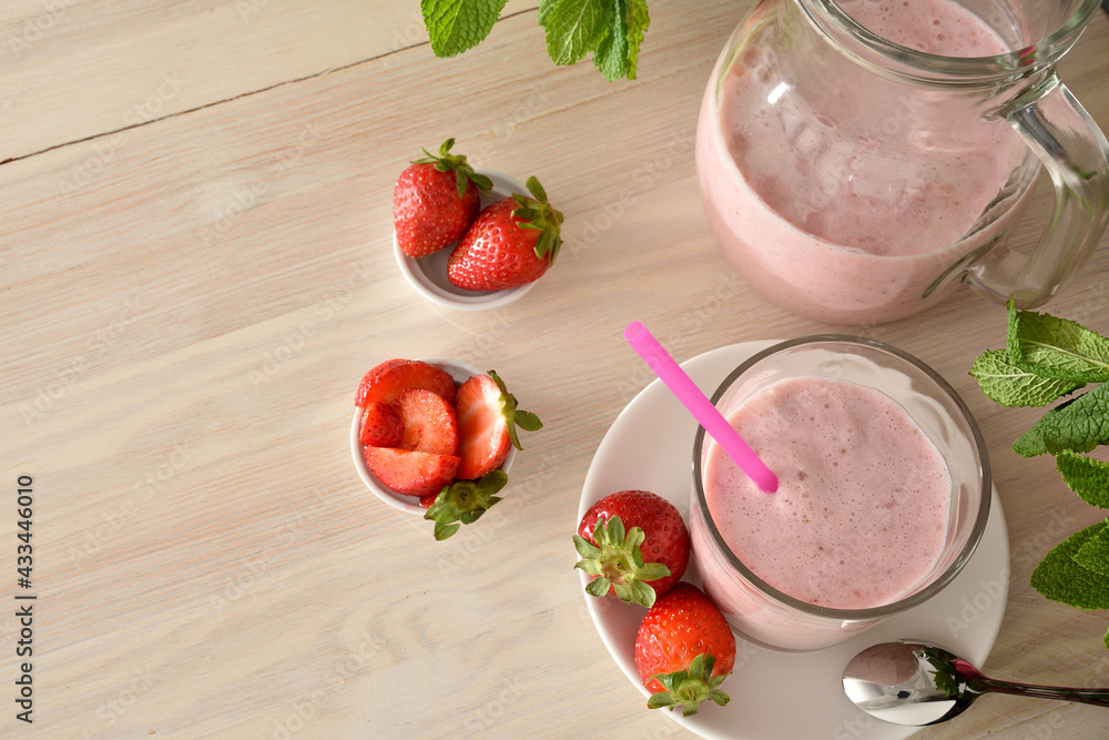 Glass and jug of strawberry milkshake on wooden table elevated Glass and jug of strawberry milkshake on wooden table elevated