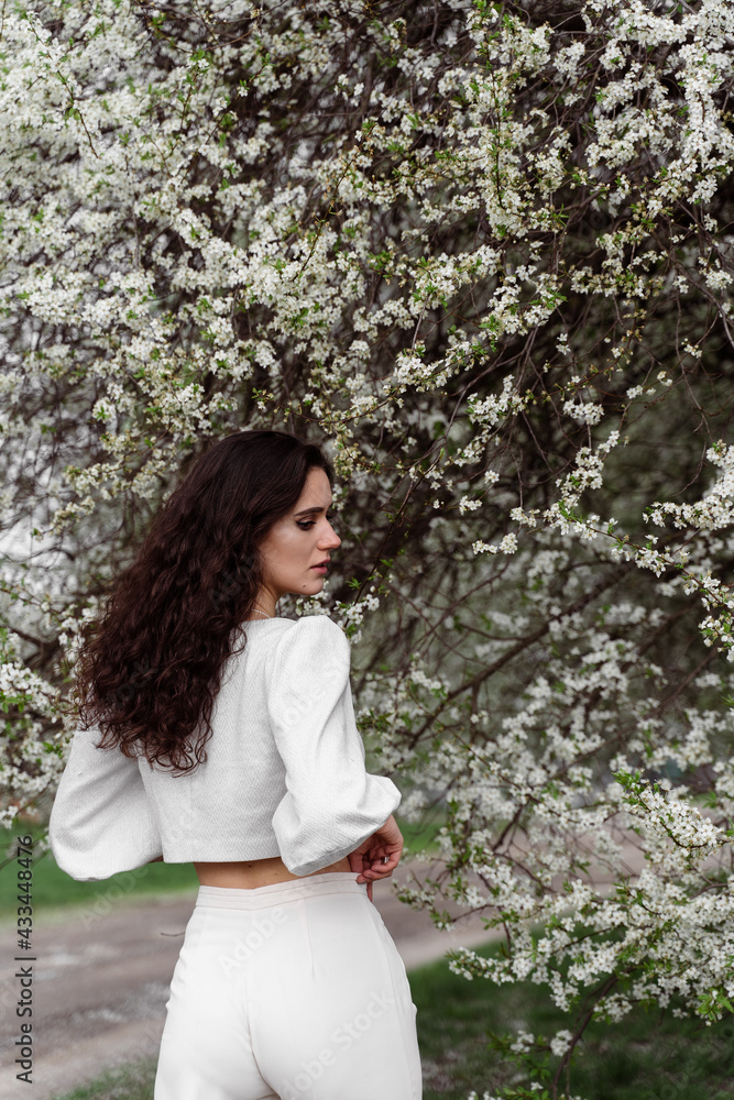 Portrait of young woman in the garden. Attractive girl weared white dress posing near blooming trees. Portrait of young woman in the garden. Attractive girl weared white dress posing near blooming trees.