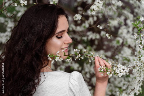 Girl touches and sniffs a branch of a white flowering tree without medical mask. Spring walking in the park.