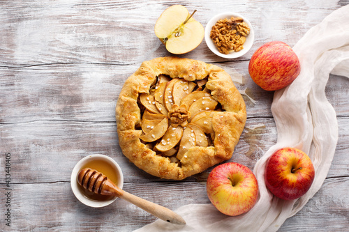 Homemade crostata pie with ripe apples, nuts and maple syrup on rustic white wooden table.