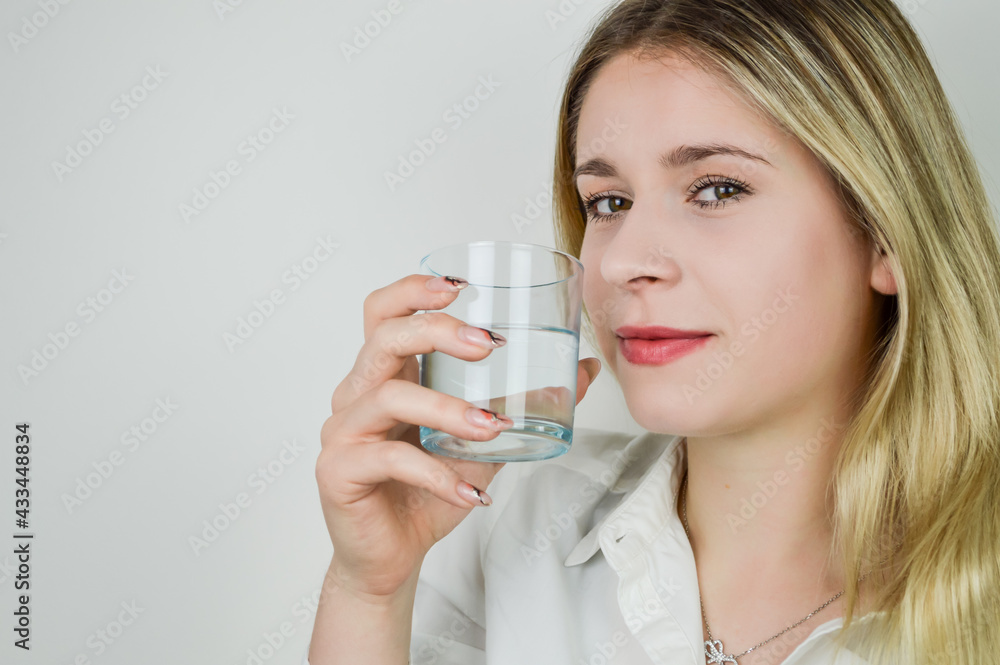 Portrait of a beautiful smiling young blonde woman holding a glass of water