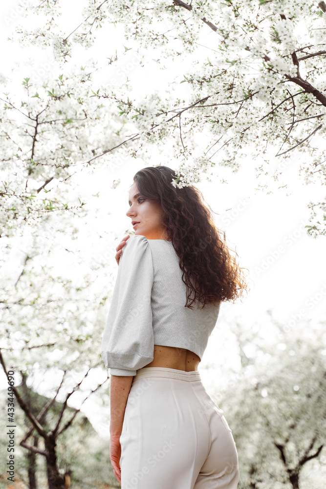 Lovely girl near blooming trees in the park. Outdoor walking in at sunny day. Lifestyle of young woman Lovely girl near blooming trees in the park. Outdoor walking in at sunny day. Lifestyle of young woman