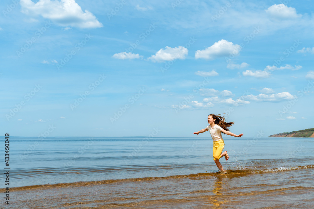 A little girl in bright yellow pants runs in the water and frolics on the beach