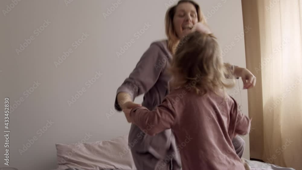 Young mother playing with her daughter on the bed in the morning