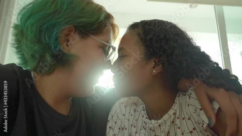 Pareja joven de lesbianas se miran cara a cara para darse un beso en contraluz