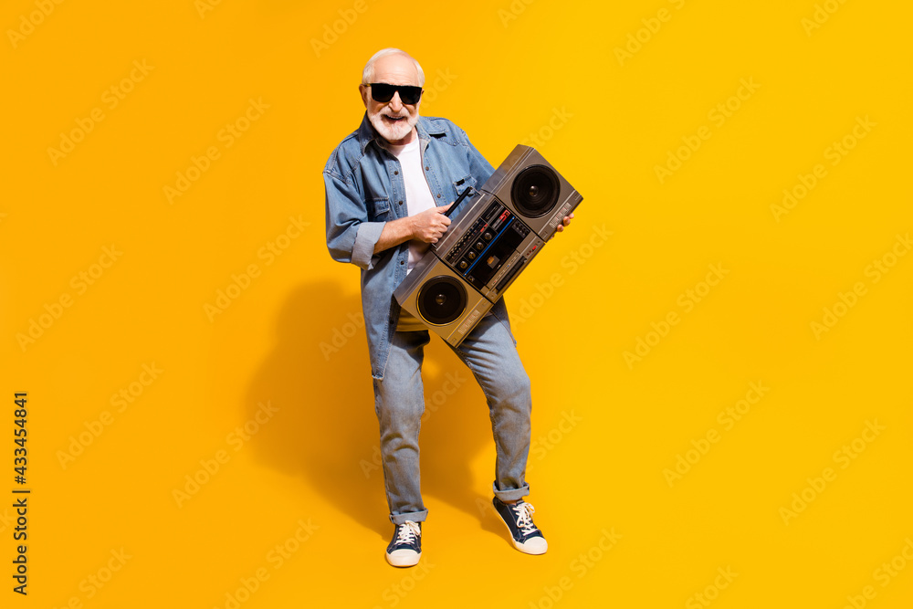 Naklejka premium Full body photo of positive carefree man hands hold boombox toothy smile isolated on yellow color background