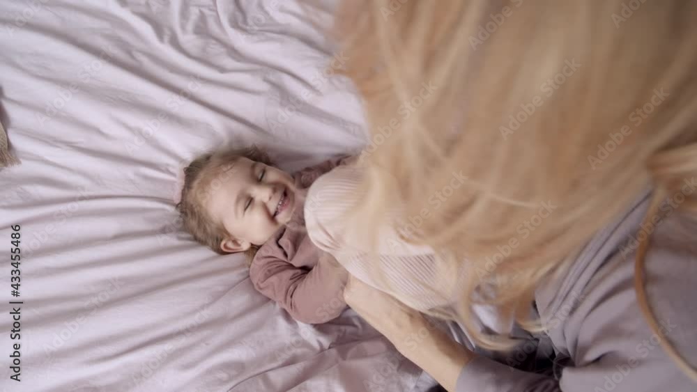 TOP VIEW: Young mom having fun with little daughter on bed in the morning TOP VIEW: Young mom having fun with little daughter on bed in the morning