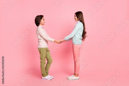 Full size profile side photo of boy and girl hold hands look at each other brother and sister isolated on pink color background