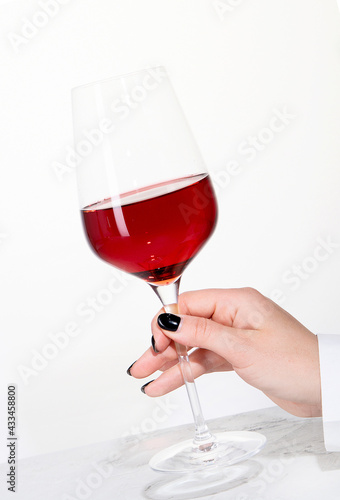 Young woman holding glass of rose wine on white background. Hand with black polish.