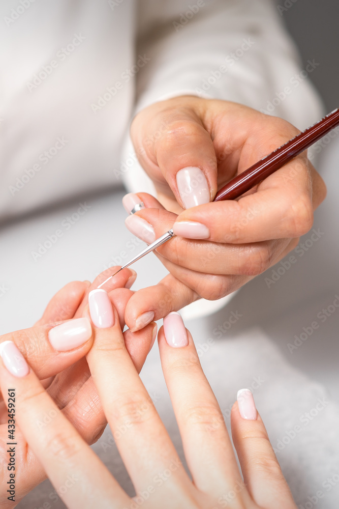 French manicure. Manicure master drawing white varnish on the nail tip with a thin brush, close up French manicure. Manicure master drawing white varnish on the nail tip with a thin brush, close up