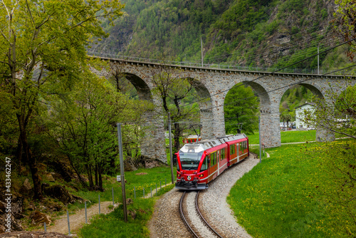 The red train on the circular viaduct bridge near Brusio on the Swiss Alps in Spring