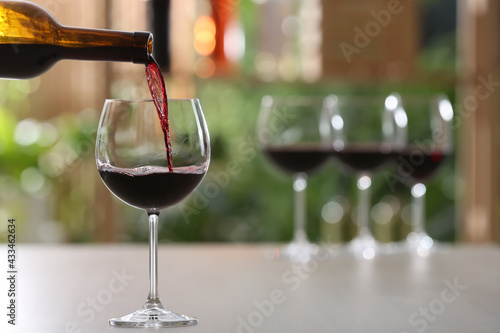 Принти на полотні Pouring red wine from bottle into glass on table against blurred background, spa