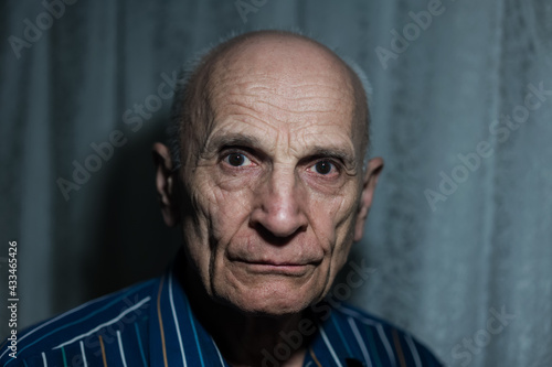 Closeup portrait of senior bald man with dark shadow behind head.