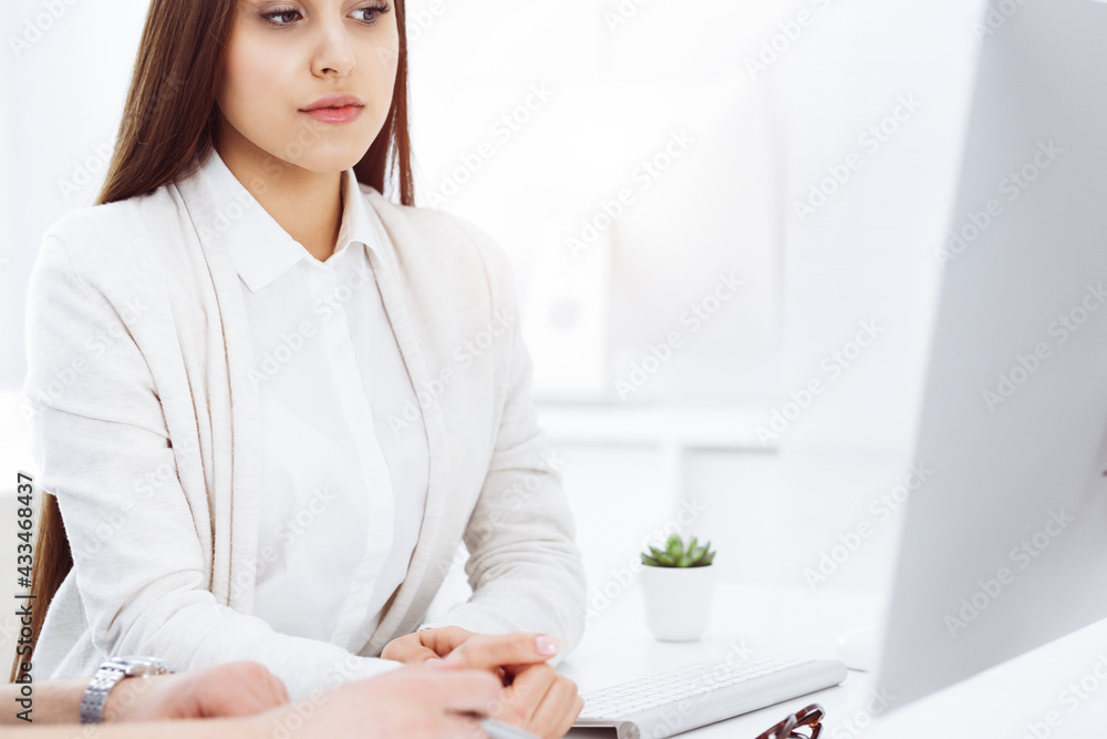 Young woman sitting at the desk with computer in sunny office. Looks like student girl or business lady communicating with casual dressed man Young woman sitting at the desk with computer in sunny office. Looks like student girl or business lady communicating with casual dressed man