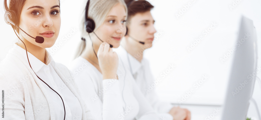Fototapeta premium Call center in sunny office. Group of diverse operators at work. Beautiful woman in headset communicating with customers of telemarketing service