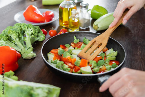 cropped view of woman mixing sliced vegetables on frying pan with spatula