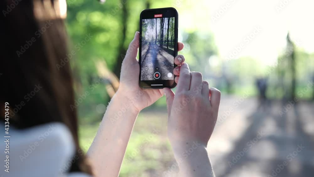 young girl in a cap shoots video on the phone in the park on a sunny spring evening slow motion young girl in a cap shoots video on the phone in the park on a sunny spring evening slow motion