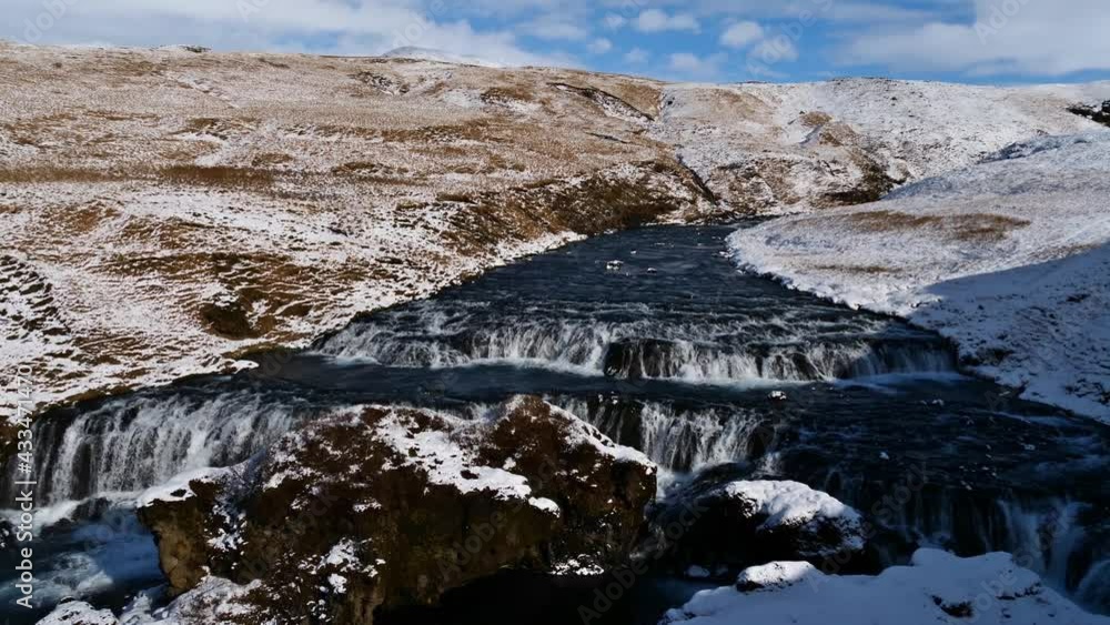 View of waterfalls of Skógá river in rocky gorge surrounded by snow-covered meadows on sunny winter day near Skógá village on the southern coast of Iceland. View of waterfalls of Skógá river in rocky gorge surrounded by snow-covered meadows on sunny winter day near Skógá village on the southern coast of Iceland.