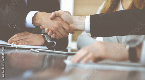 Unknown businessmen shaking hands above the glass desk in a modern office, close-up. Unknown business people at meeting. Teamwork, partnership and handshake concept
