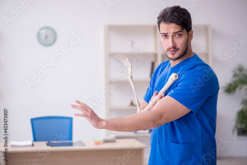 Young male doctor holding human skeleton's hand
