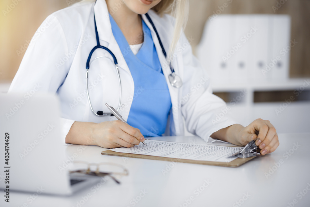 Unknown woman-doctor at work filling up medication history record form in sunny clinic, close-up Unknown woman-doctor at work filling up medication history record form in sunny clinic, close-up