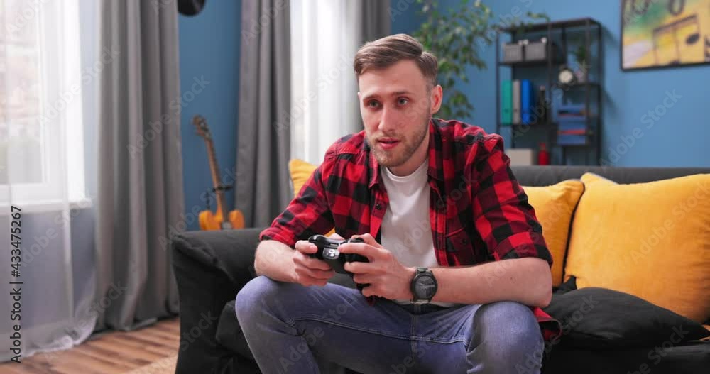 Collage student boy is enjoying video game using controller concentrated on interesting activity in apartment. Teenagers lifestyle and leisure time at home concept. Collage student boy is enjoying video game using controller concentrated on interesting activity in apartment. Teenagers lifestyle and leisure time at home concept.