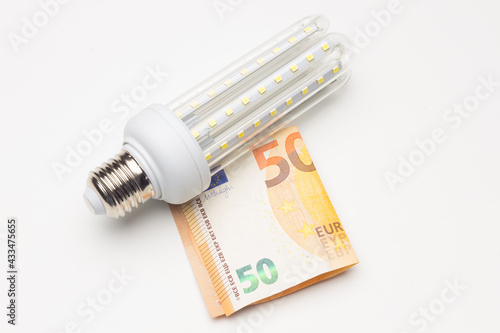 Energy-saving light bulb and money on white background