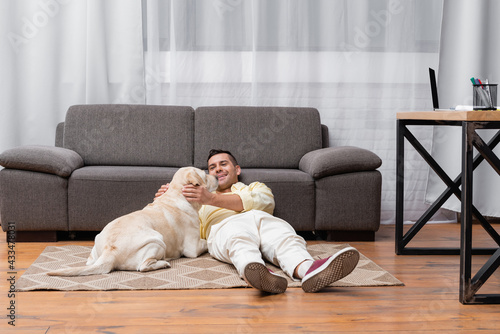 young man having fun with labrador dog while lying on floor near sofa