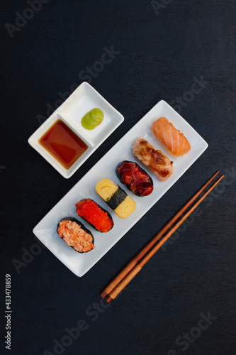 The sushi set is a famous Japanese dish, put on a ceramic plate, beautifully arranged on a black background.