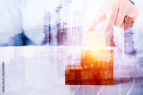 Double exposure image concept, hand holding wooden block idea business industrial technology future plant and enegry graphic design. Oil, gas and petrochemical refinery factory with background.