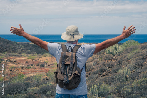 Rear view of senior man traveler enjoying outdoors trekking, looking at horizon over sea with open arms