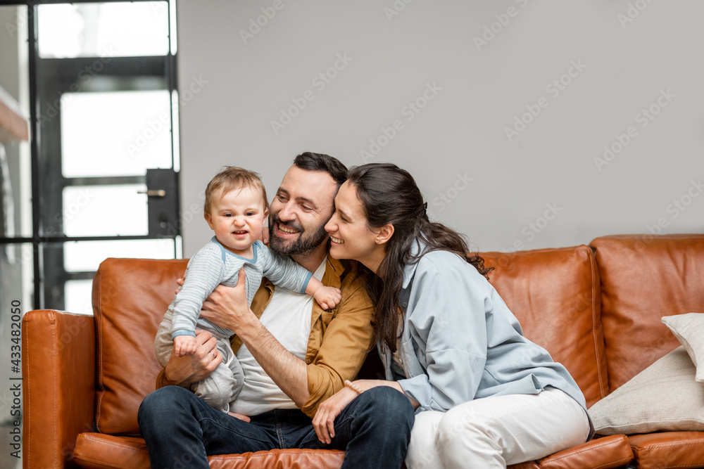Happy father, mother and little son are playing on sofa in living room. Child care and parenting. Love and harmony in family relationships.