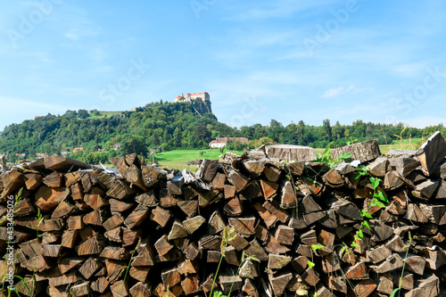 Riegersburg castle in Austria towering above the area. There are wooden logs pilled up in front. Clear blue sky above the castle. The massive fortress was build on the rock. Middle ages