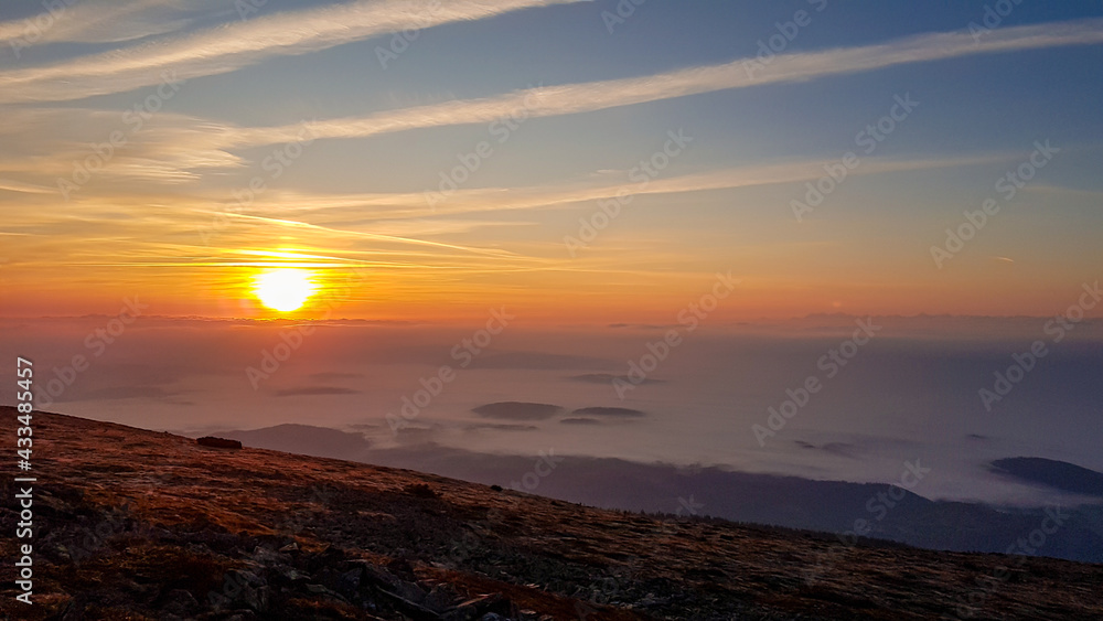 A panoramic view on sun rising above the horizon from the top of Babia Gora in Poland. Thick clouds below. The sky is pink and orange. A few small peaks popping out from the clouds. Freedom. Daybreak
