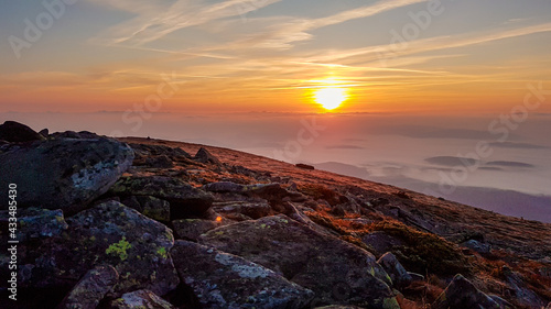 A panoramic view on sun rising above the horizon from the top of Babia Gora in Poland. Thick clouds below. The sky is pink and orange. A few small peaks popping out from the clouds. Freedom. Daybreak photo