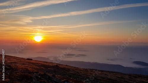 A panoramic view on sun rising above the horizon from the top of Babia Gora in Poland. Thick clouds below. The sky is pink and orange. A few small peaks popping out from the clouds. Freedom. Daybreak